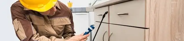 Roach exterminator applying treatment under kitchen cabinets in Provo, UT