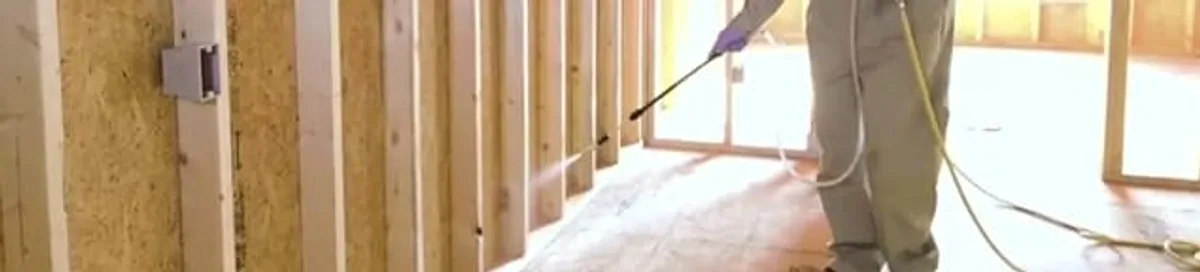 Termite treatment technician applying spray along framing and unfinished walls in Provo, UT