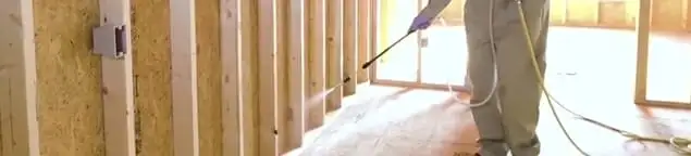 Termite treatment technician applying spray along framing and unfinished walls in Provo, UT